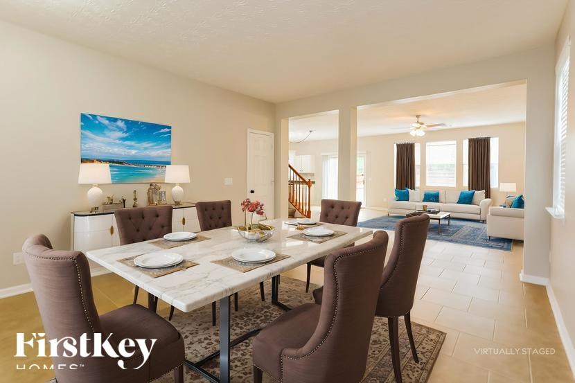 A dining room with a table set for six and a painting of a beach scene on the wall.