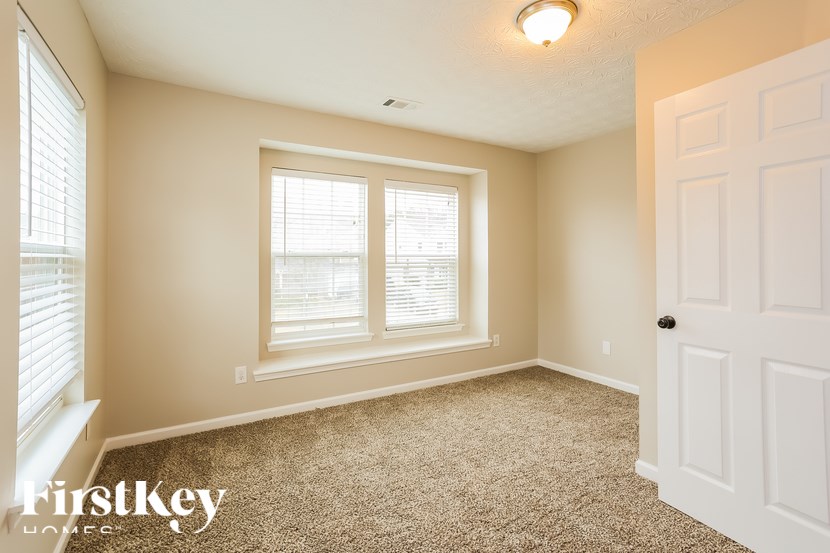 A room with a carpeted floor, a window with blinds, and a white door.
