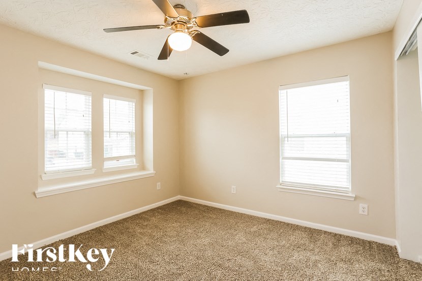 A room with a carpet floor, a ceiling fan, and two windows.