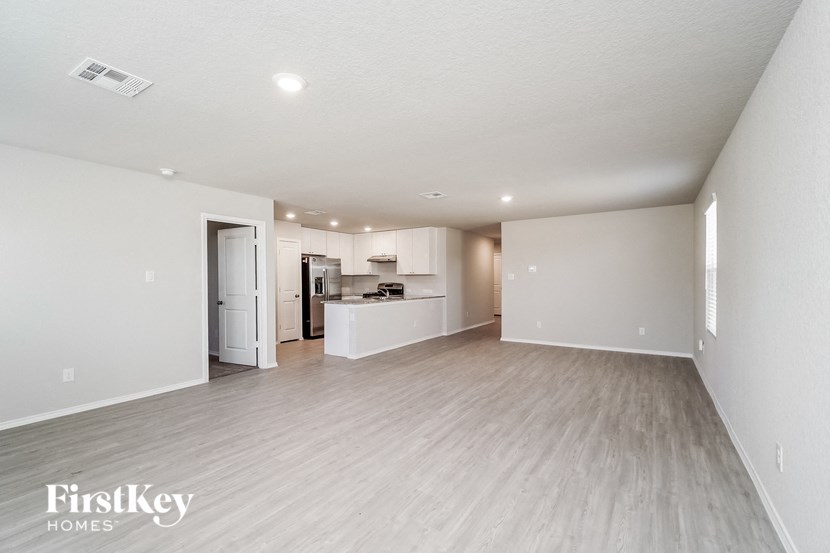 a spacious living room and kitchen with white walls and wood flooring