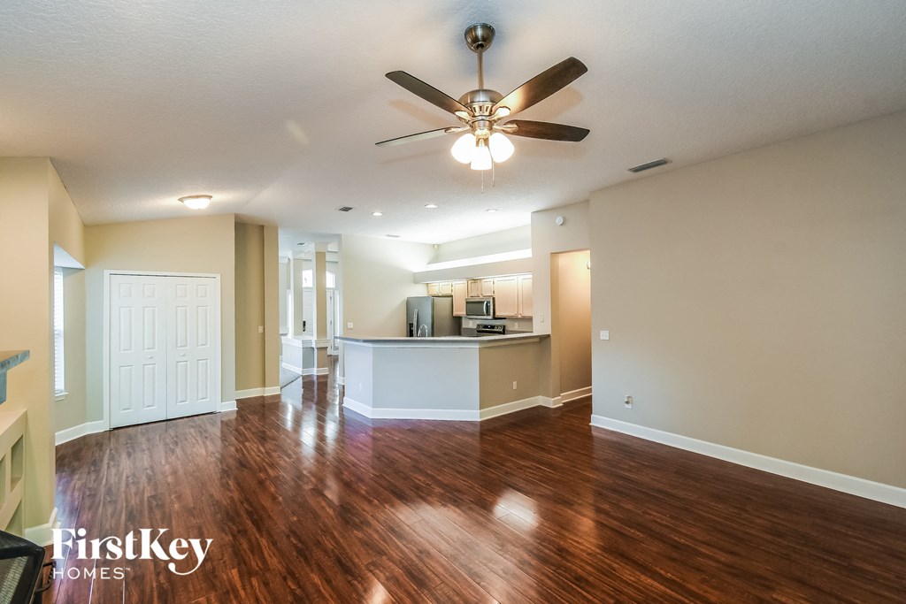 an empty living room with a ceiling fan and a kitchen