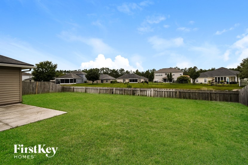 A grassy field with a wooden fence and houses in the background.