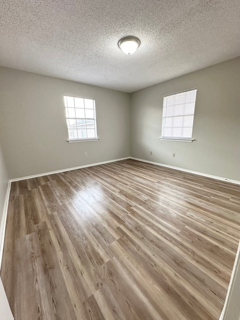 an empty living room with wood flooring and two windows