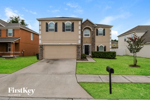 a beige and brick house with a driveway and lawn
