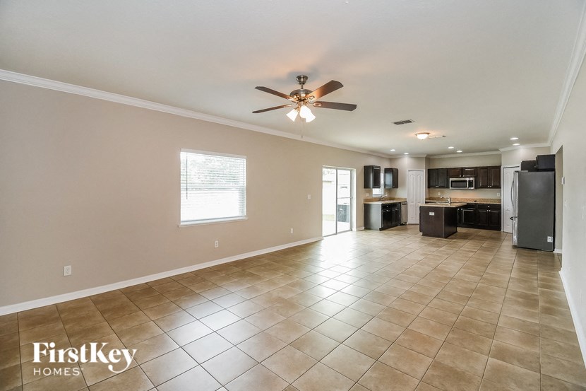 an empty living room with a ceiling fan and a kitchen