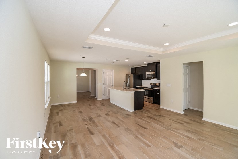 A spacious room with wooden flooring and a kitchen area in the background.