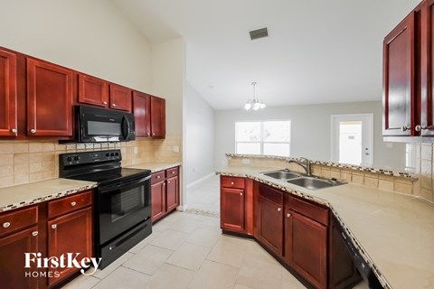 A kitchen with red cabinets and black appliances.