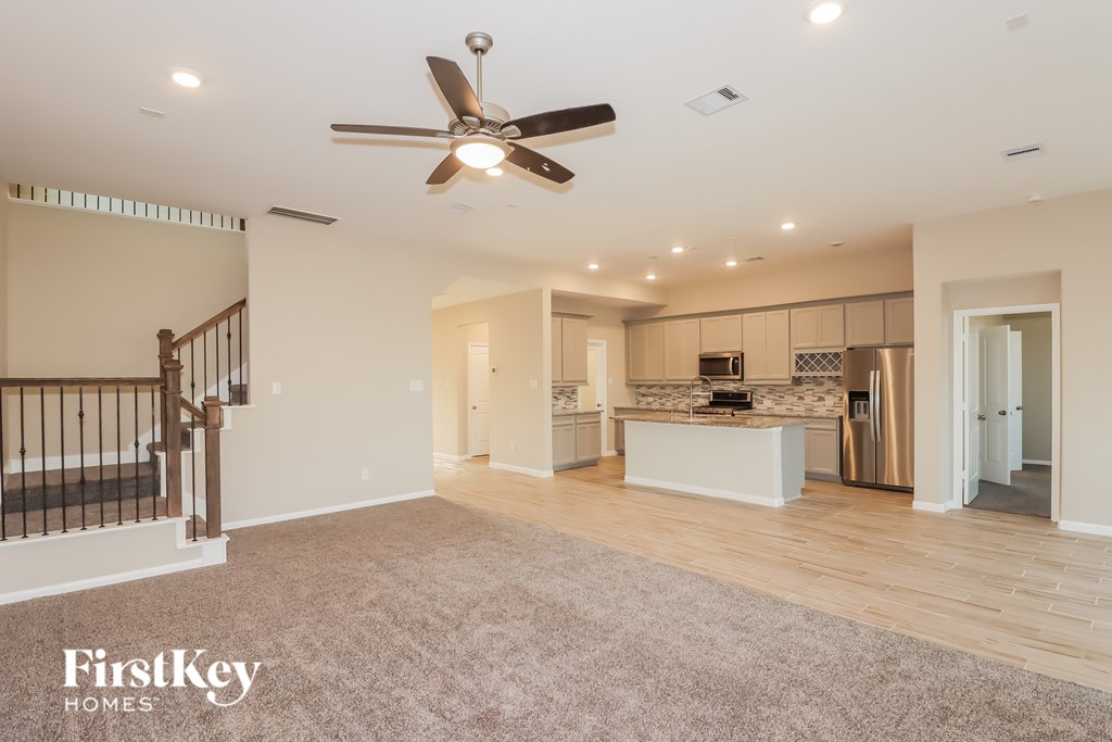 A spacious living room with a ceiling fan and a staircase on the left side.