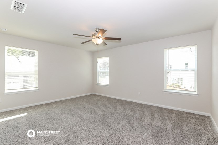 an empty living room with a ceiling fan and two windows