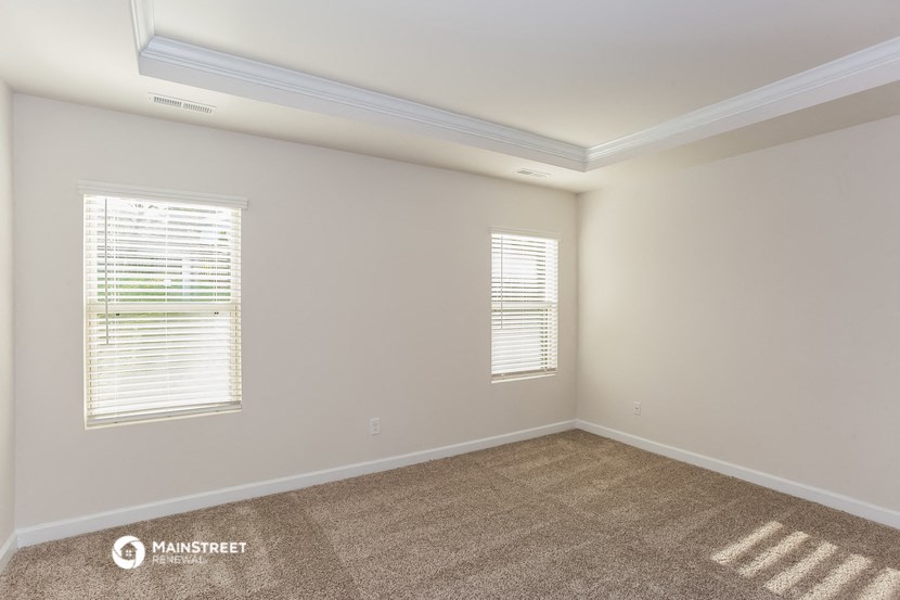 the living room of a house with carpet and two windows