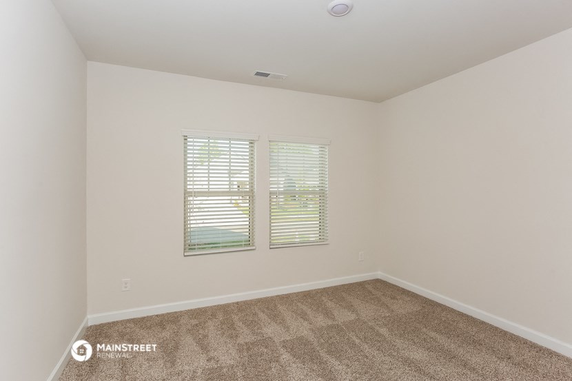 a spacious living room with carpet and two windows