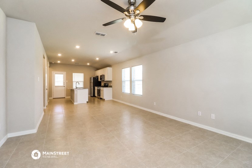 an empty living room with a ceiling fan and a kitchen