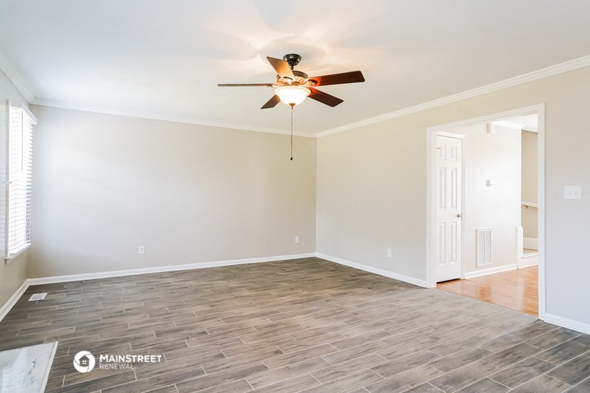 the spacious living room with wood flooring and a ceiling fan