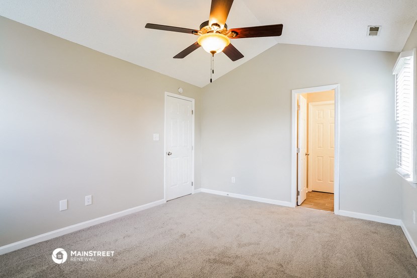 an empty living room with a ceiling fan and a door to a hallway