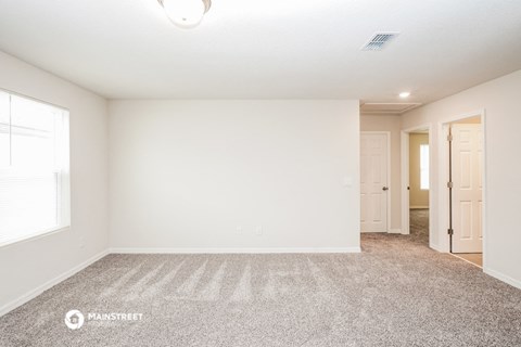 a spacious living room with carpet and a door to a hallway