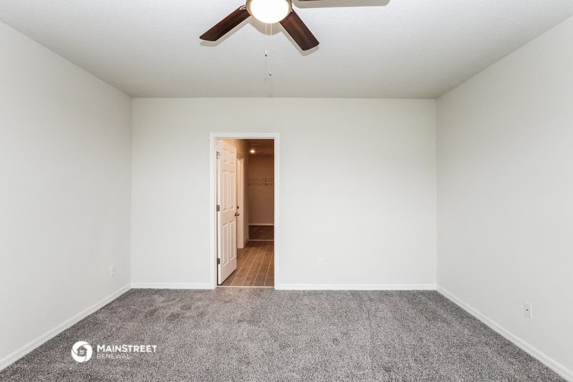 the living room of an apartment with carpet and a ceiling fan
