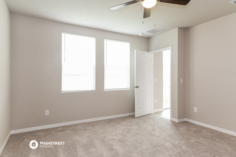 an empty living room with a ceiling fan and three windows