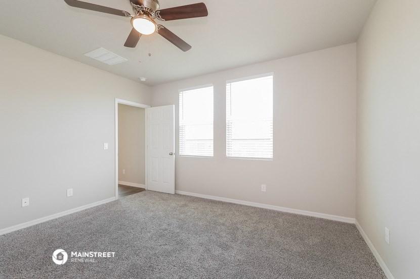 an empty room with a ceiling fan and three windows