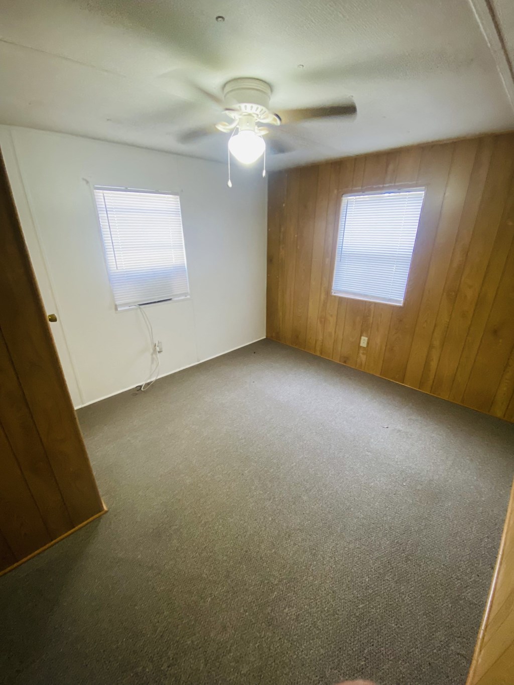 an empty room with a ceiling fan and two windows