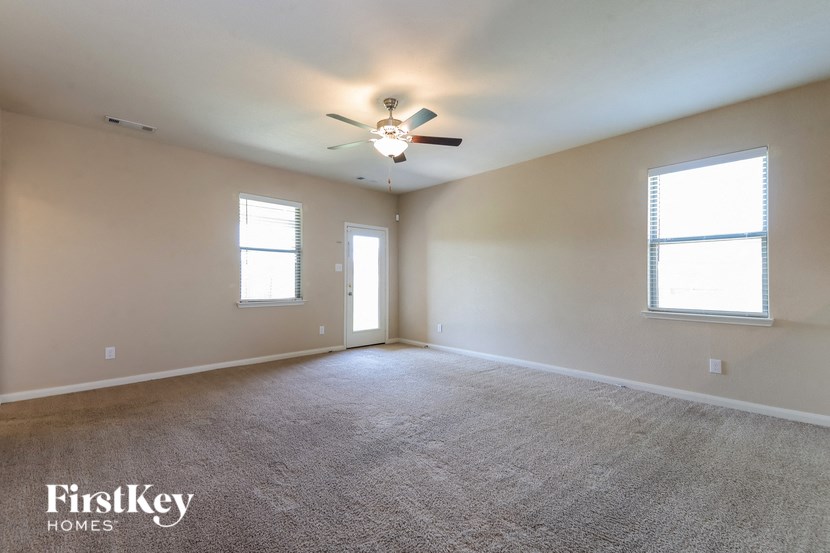 an empty living room with a ceiling fan and two windows