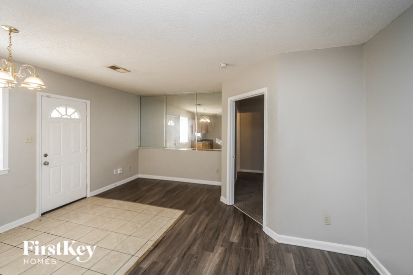 an empty living room with a door to the bathroom and a hallway to the kitchen