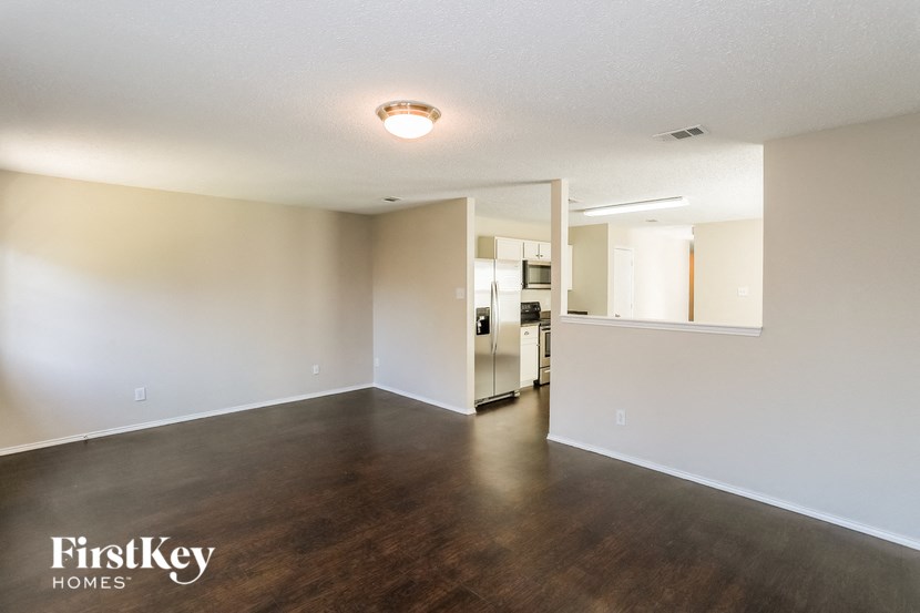 an empty living room and kitchen with wood flooring and white walls