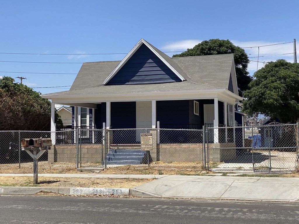 a small house with a fenced in yard behind a chain link fence