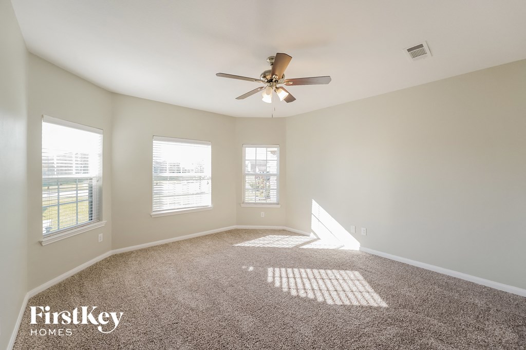 A spacious room with a ceiling fan and three windows.