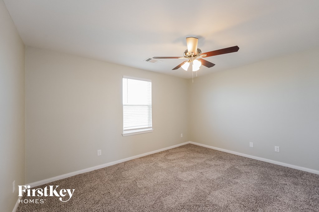 A carpeted room with a ceiling fan and a window.