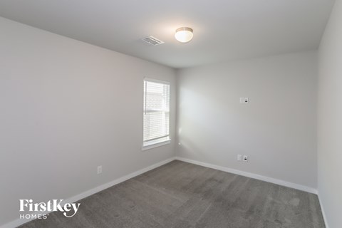 a bedroom with white walls and gray carpet and a window