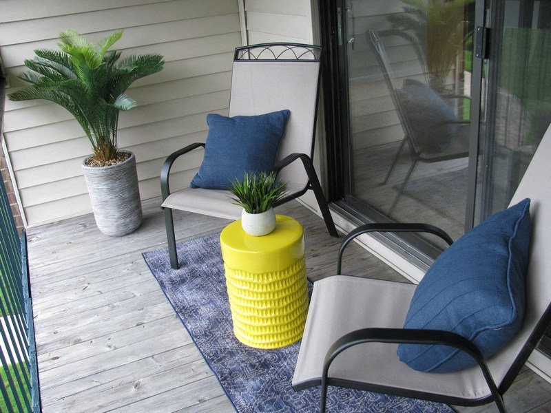 a porch with two chairs and a yellow vase with plants