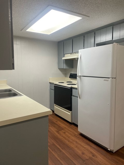 A white refrigerator stands in a kitchen with wooden floors and white walls.