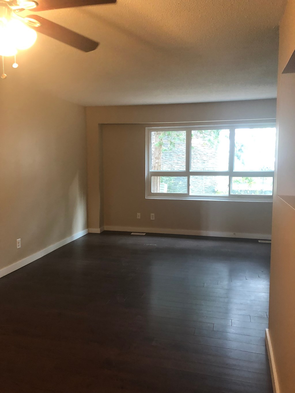 an empty living room with a large window and wooden floors