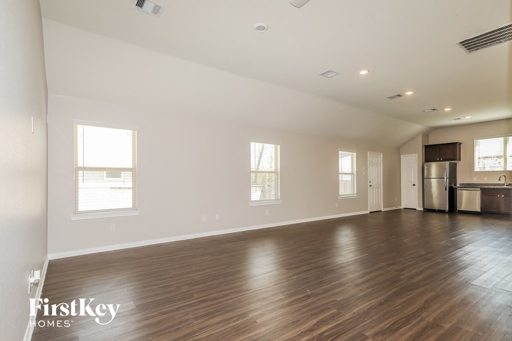 an empty living room with wood flooring and a kitchen
