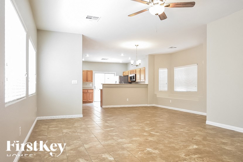 A spacious room with a fan and a kitchen area in the background.