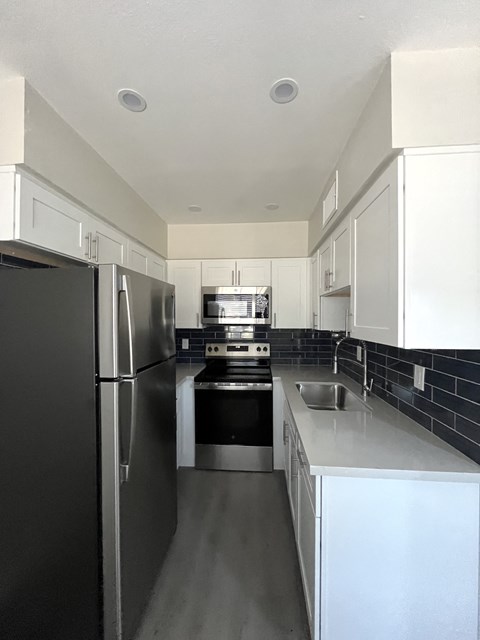 an empty kitchen with stainless steel appliances and white cabinets