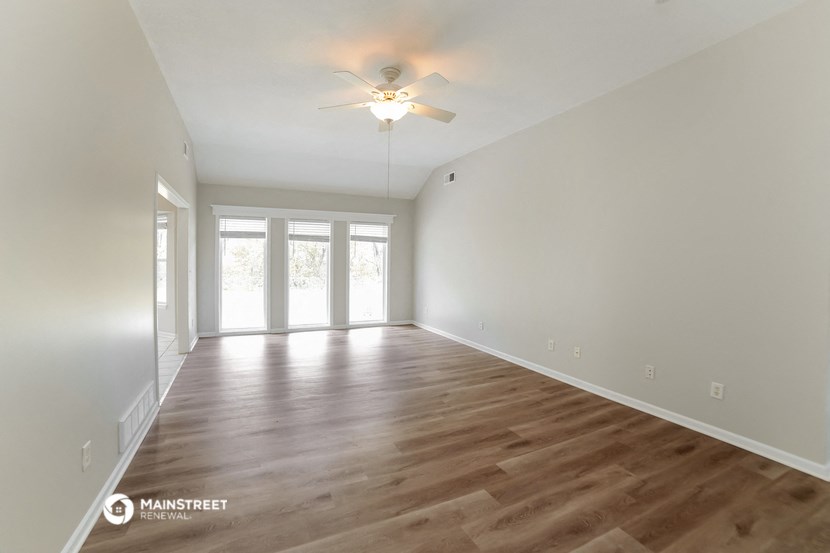 the spacious living room with wood flooring and a ceiling fan