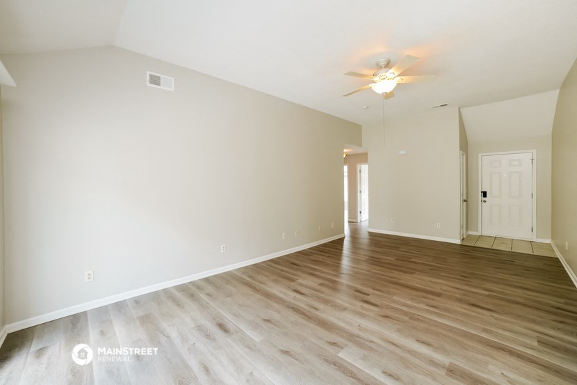 the spacious living room with wood flooring and a ceiling fan