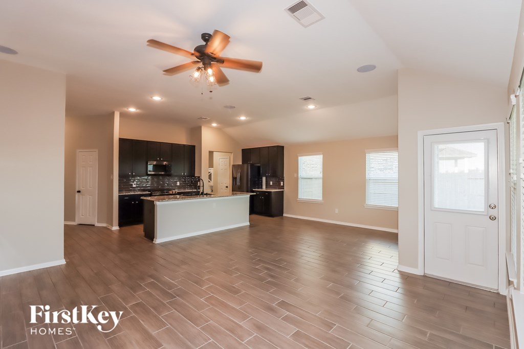 A spacious living room with a kitchen in the background and a ceiling fan above.