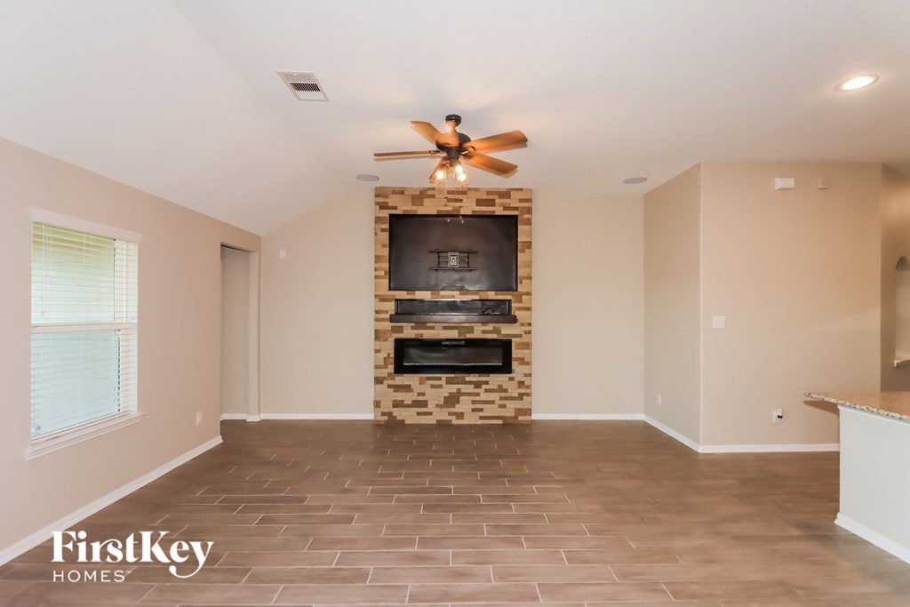 A spacious living room with a stone fireplace and a ceiling fan.