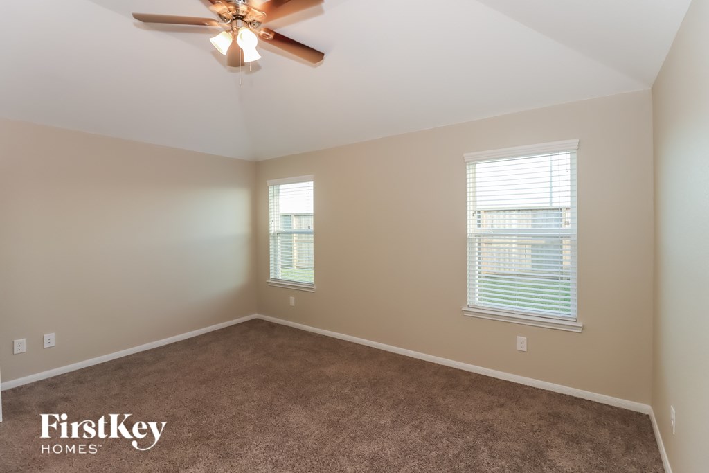 A room with a ceiling fan and two windows.