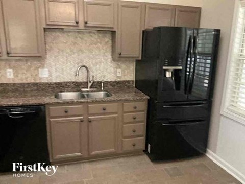A black refrigerator sits next to a sink in a kitchen.