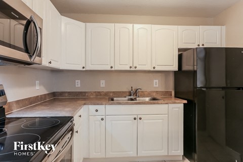 A kitchen with white cabinets and a black refrigerator.