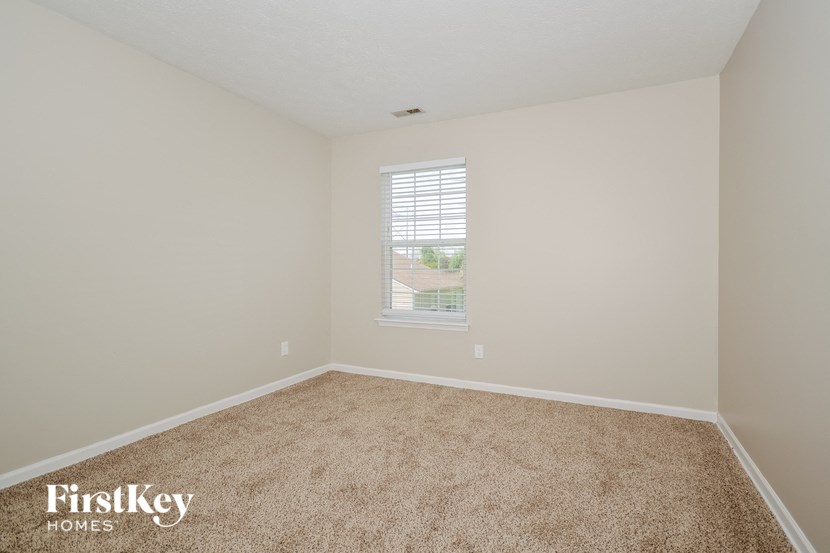 a spacious bedroom with carpet and a window