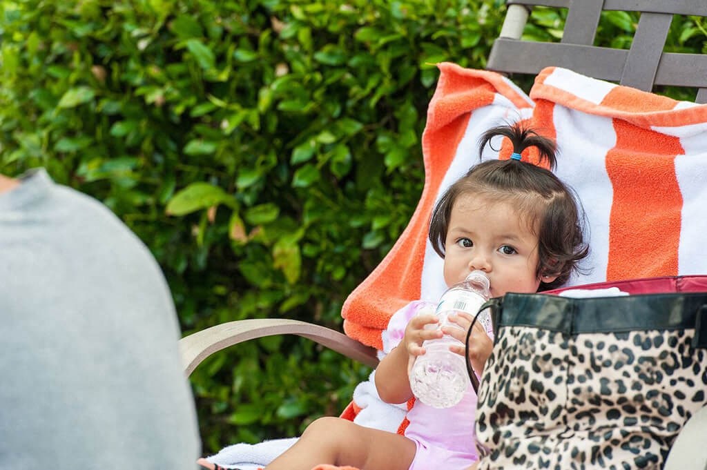 a little girl sitting in a chair drinking a bottle of water