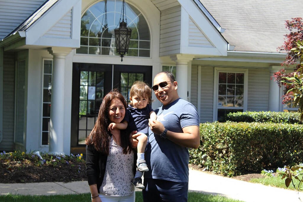 a man and woman holding a child in front of a house