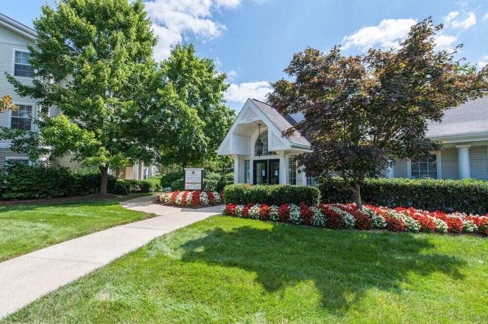 a sidewalk in front of a white house with trees and flowers