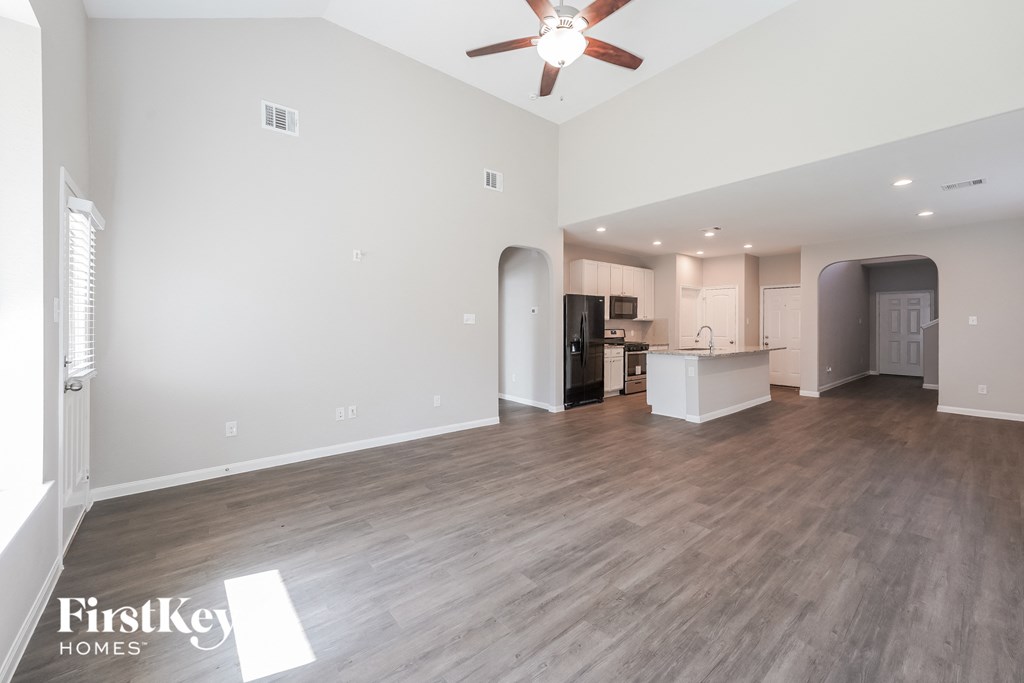 an empty living room with a ceiling fan and a kitchen