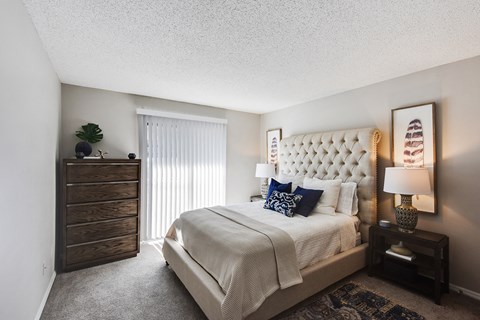 A bedroom with a large bed, a wooden dresser, and a lamp on a side table.