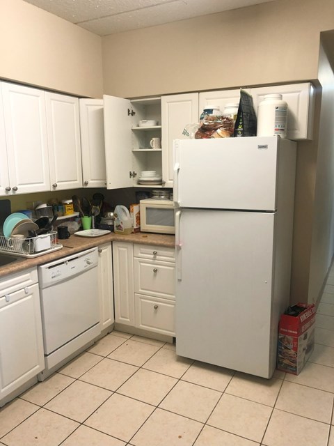 A white refrigerator is in a kitchen with white cabinets.
